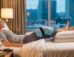 A post knee replacement patient sitting comfortably in an airplane aisle seat with their leg gently extended and a compression stocking visible, representing safe travel after surgery