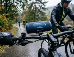 A waterproof Bluetooth speaker mounted on a bicycle handlebar during a rainy outdoor ride